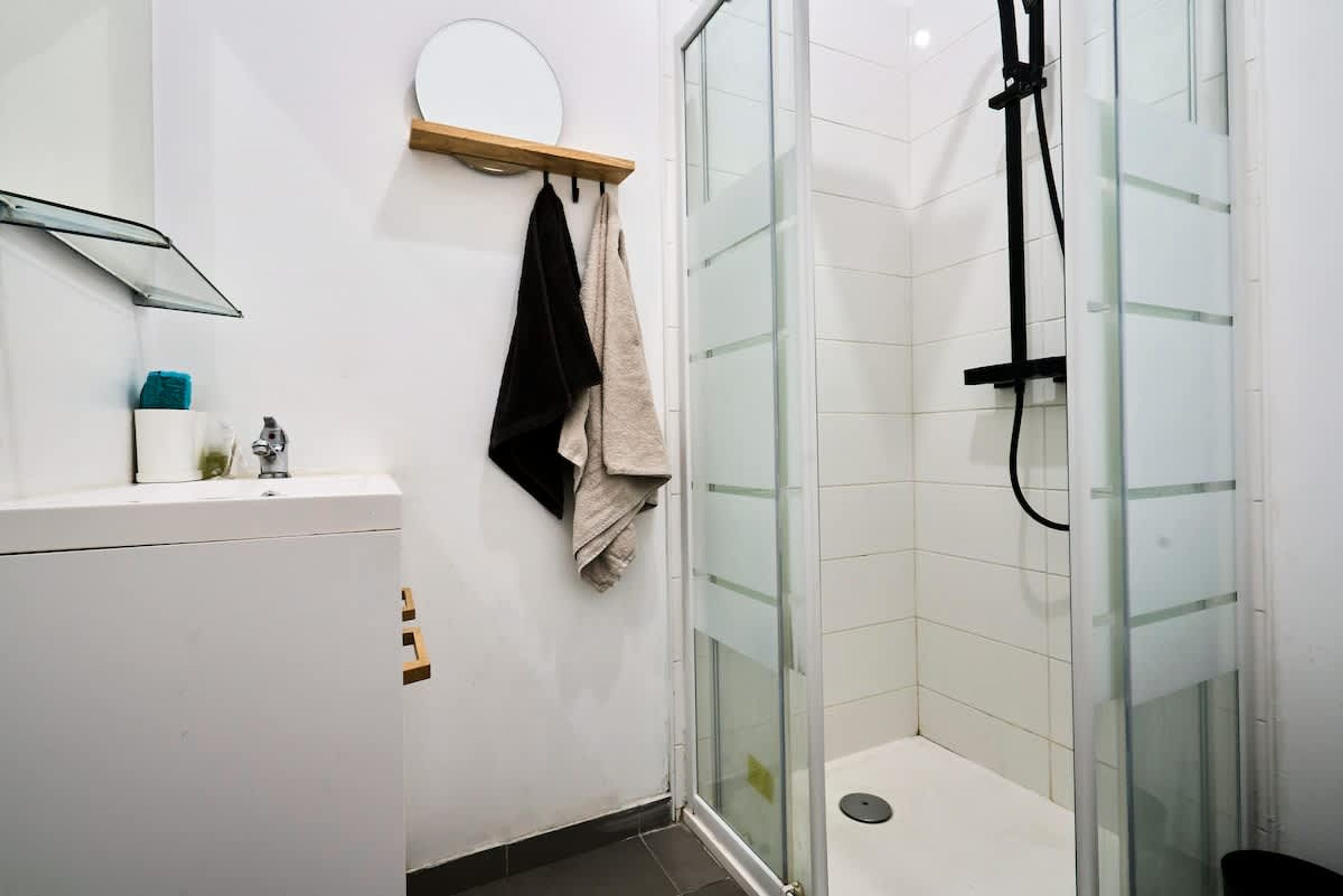 A bathroom with a glass shower enclosure, a white sink, and a towel rack with towels.