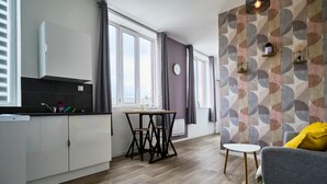 A compact kitchen with a dining area, a grey sofa, and a patterned wall. - En D Placement 5 Calme et Lumineux (Tourcoing)