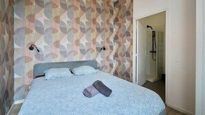 A bedroom with a bed, a shower area, and a patterned wall. - En D Placement 5 Calme et Lumineux (Tourcoing)