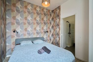 Une chambre avec un lit, un espace douche et un mur décoré d’un motif.
