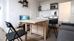 Pieni, käytännöllinen keittiö, jossa on puinen pöytä, mustat tuolit, televisio, mikroaaltouuni ja uuni.