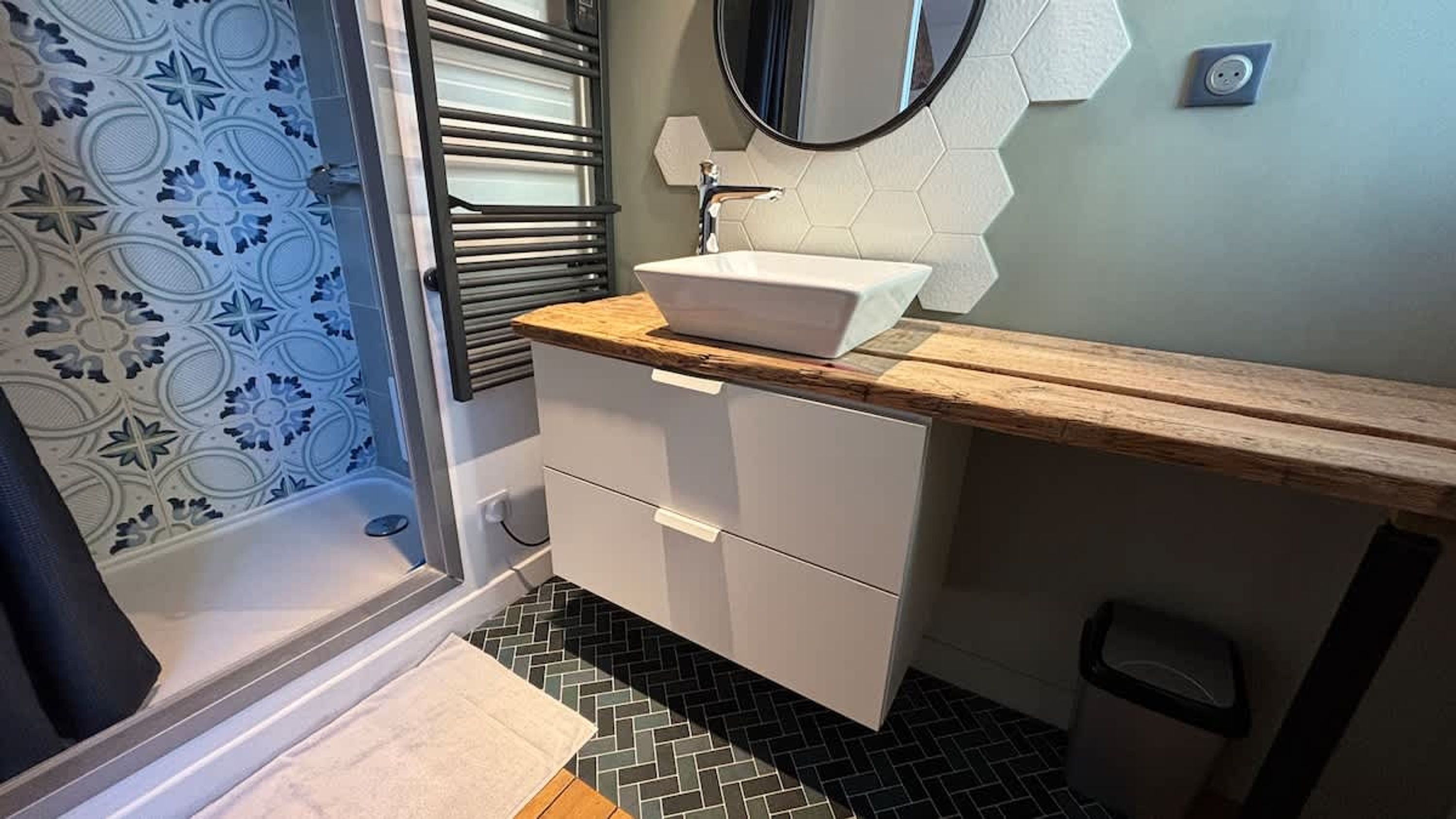 Een badkamer met een douche, een wastafel met een houten aanrechtblad, een spiegel en een betegelde vloer.