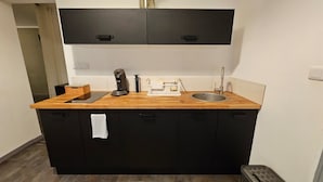 A compact kitchen with a wooden countertop, a coffee maker, a sink, and black cabinets. - Appartement Cosy Grand Place (Arras)