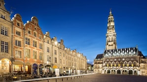 A historic building with a prominent tower, a paved square, and traditional architecture. - Appartement Cosy Grand Place (Arras)