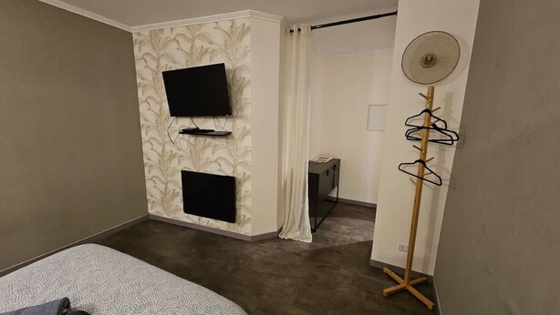 A room with two mounted TVs, a wooden coat rack, a fan, and a door leading to another room. - Appartement Cosy Grand Place (Arras)