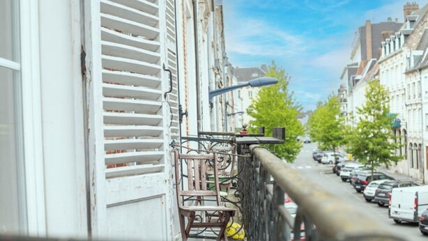 Une rue étroite bordée de voitures garées, un vélo jaune et un immeuble aux volets blancs.