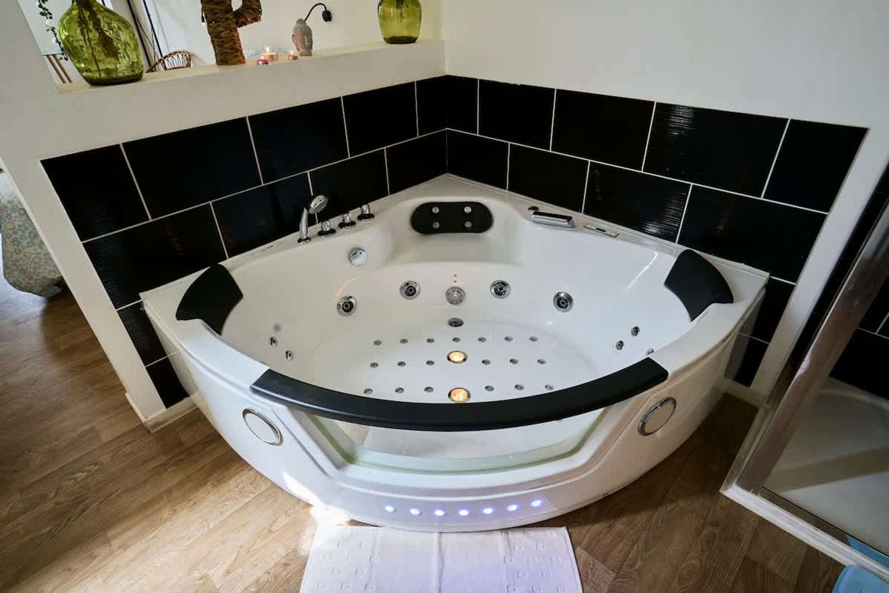 A corner bathroom with a freestanding bathtub, black and white tiled walls, and a wooden floor.