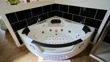 A corner bathroom with a freestanding bathtub, black and white tiled walls, and a wooden floor.