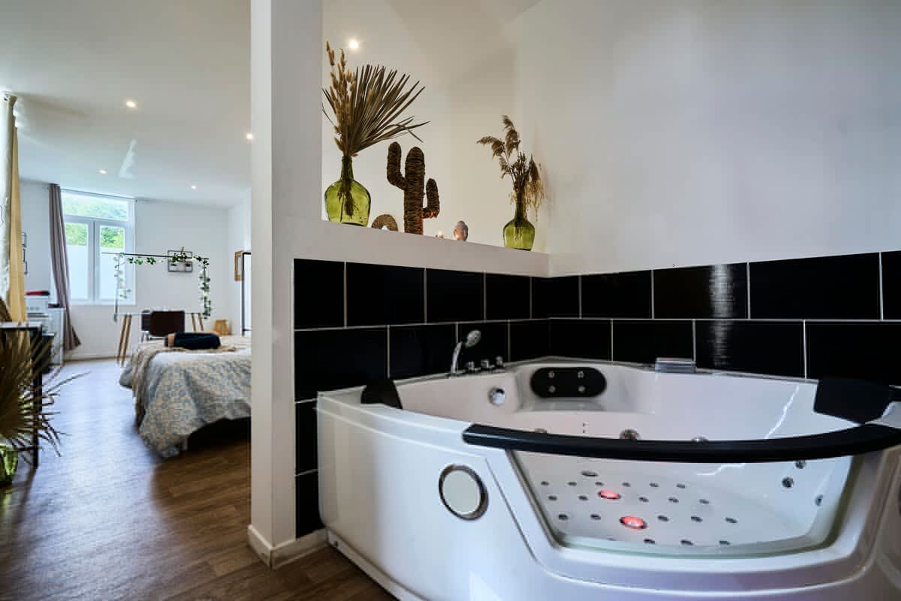 A modern bathroom with a white bathtub, black tiles, and decorative plants.