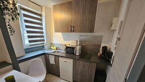 A compact kitchen with a microwave, toaster, and coffee maker, a small sink, and a white chair. - Le Studio du Th tre (Arras)
