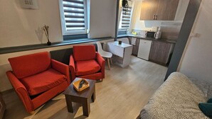 A compact living space with a kitchenette, two red armchairs, a small table with a remote, and a patterned sofa. - Le Studio du Th tre (Arras)