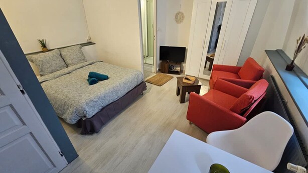 A bedroom with a bed, a TV, a red sofa, a white chair, and a small table. - Le Studio du Th tre (Arras)
