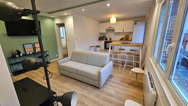 A compact living space with a sofa, a dining area with stools, a kitchenette, and a large window. - La Citadine Hyper Centre Garage 2 Chambres (Arras)
