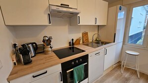 A modern kitchen with a black induction cooktop, a built-in oven, a stainless steel sink, and a window providing a view. - La Citadine Hyper Centre Garage 2 Chambres (Arras)