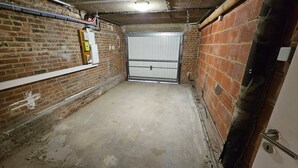 A brick-walled corridor with a concrete floor, a white door, and a fire alarm on the left wall. - La Citadine Hyper Centre Garage 2 Chambres (Arras)