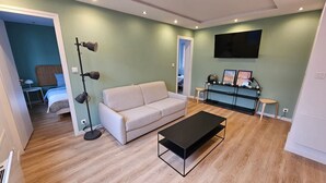 A modern living room with a sofa, a coffee table, a floor lamp, and a TV mounted on the wall. - La Citadine Hyper Centre Garage 2 Chambres (Arras)