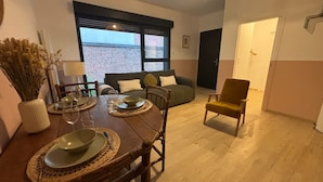 A dining area with a wooden table set for four, a sofa, and a single armchair. - Le Citadin Appartement Arras Centre 6 Personnes (Arras)