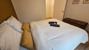 A bed with white bedding and two pillows, a wooden bench, and a door leading to a bathroom. - Le Citadin Appartement Arras Centre 6 Personnes (Arras)