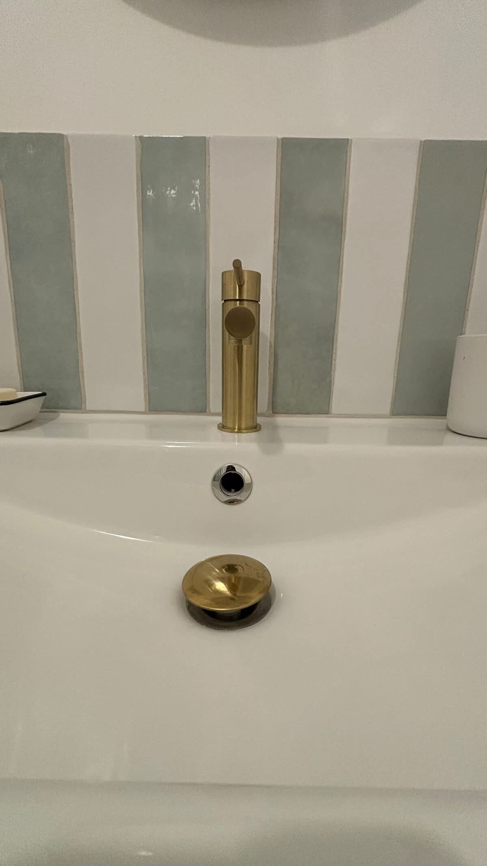 A bathtub with a gold faucet and drain, set against a wall with vertical stripes.