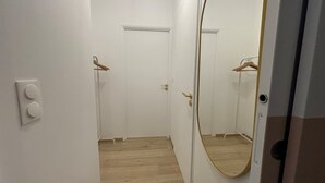 A narrow hallway with a wooden floor, a white door, and a mirror reflecting the door and a hanging garment. - Le Citadin Appartement Arras Centre 6 Personnes (Arras)