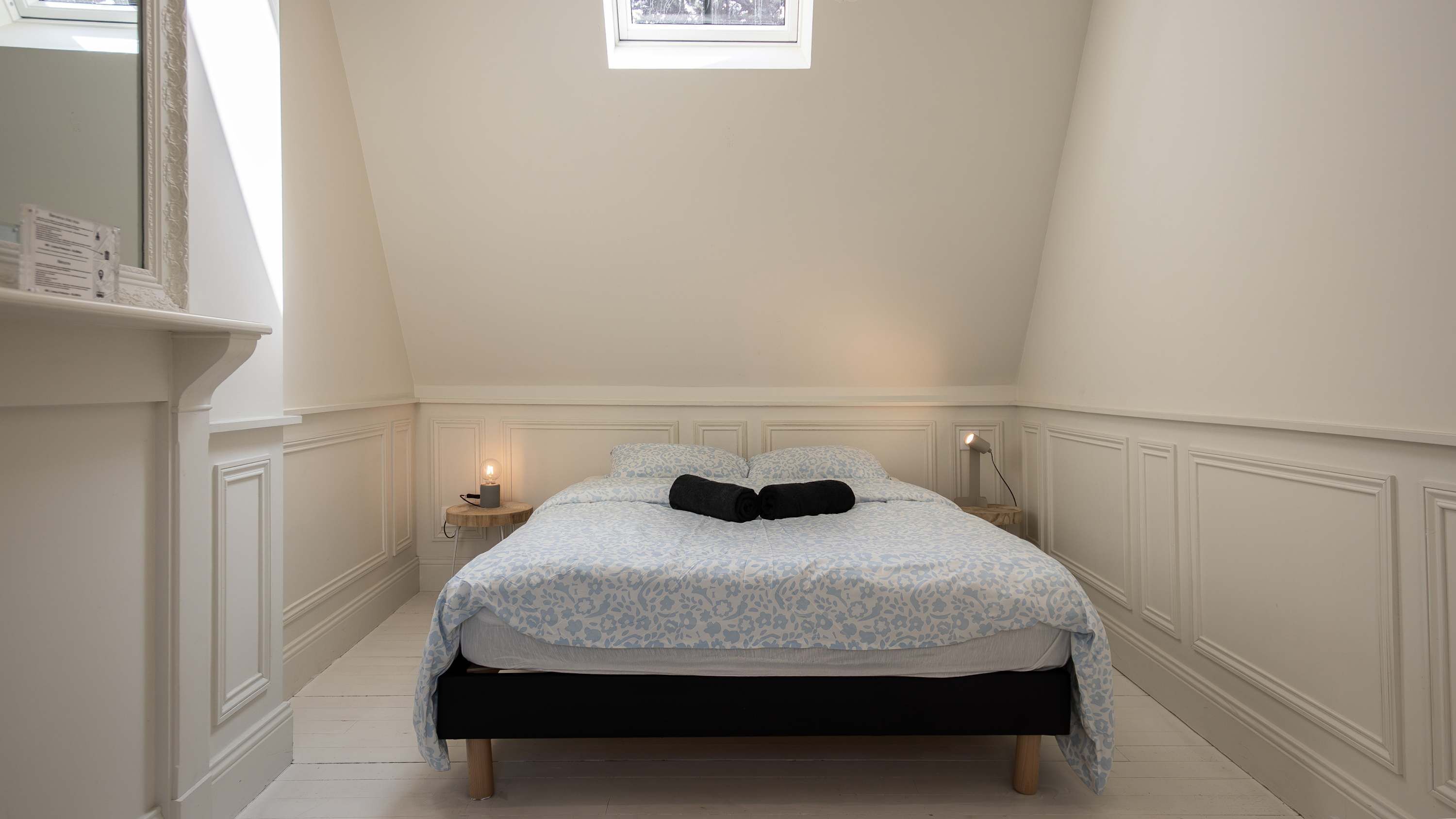 A bedroom with a bed, bedside lamps, a small table, and a window.