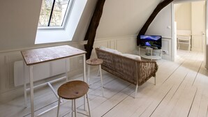 A room with a sloped ceiling, a television on a stand, a small table with stools, and a wicker sofa. - T2 de la Prefecture in Arras (Arras)