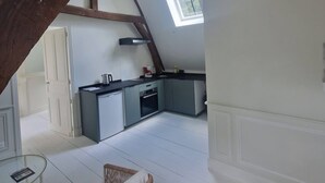 A loft-style room with exposed wooden beams, a kitchenette, a glass table, and a wicker chair. - T2 de la Prefecture in Arras (Arras)