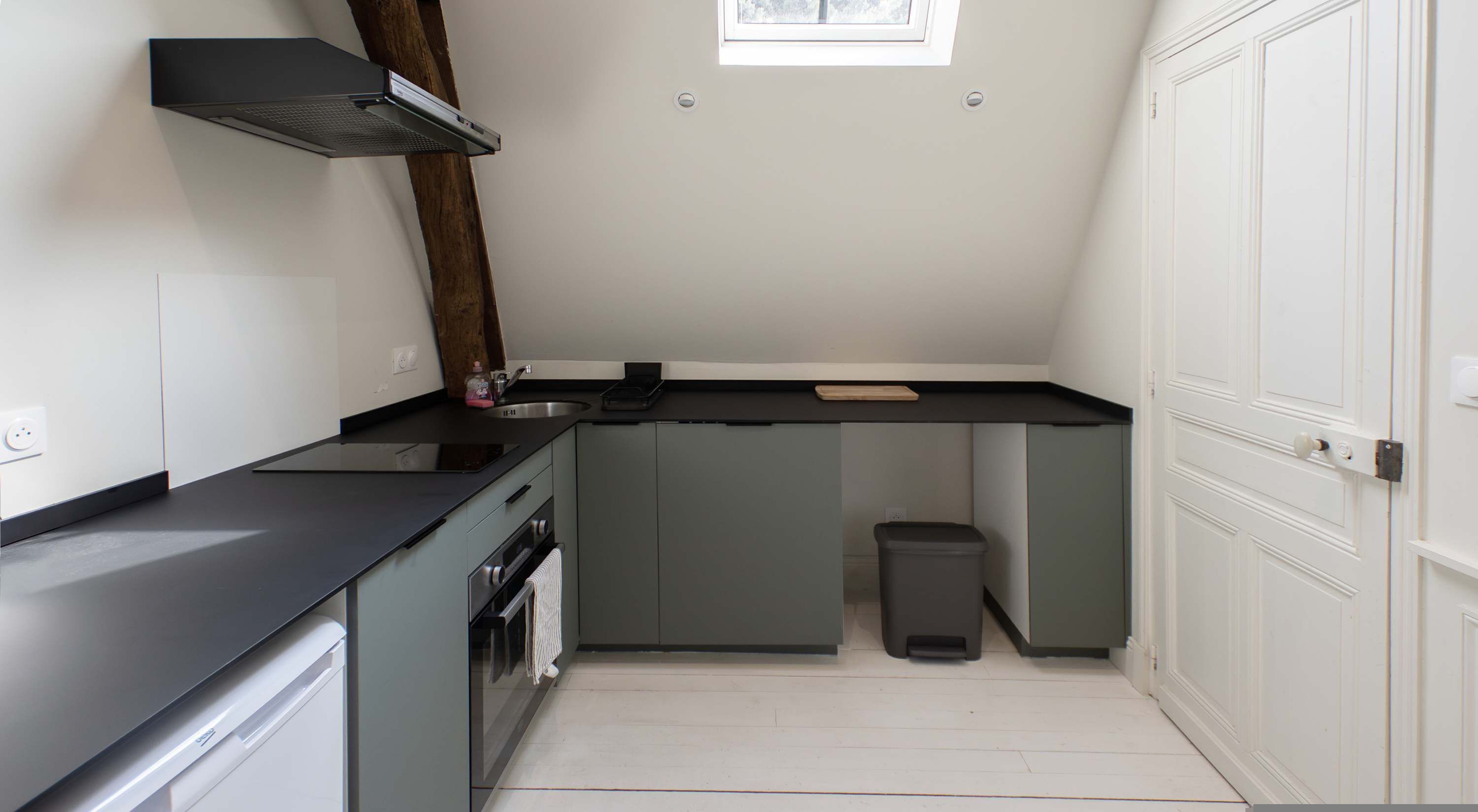 A compact kitchen with a built-in oven, a sink, and a trash bin.