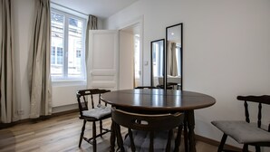 Een eetkamer met een ronde tafel, twee stoelen, een spiegel en een uitzicht door een raam.