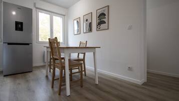 A kitchen with a refrigerator, a dining table, and two chairs. There are three framed artworks on the wall.