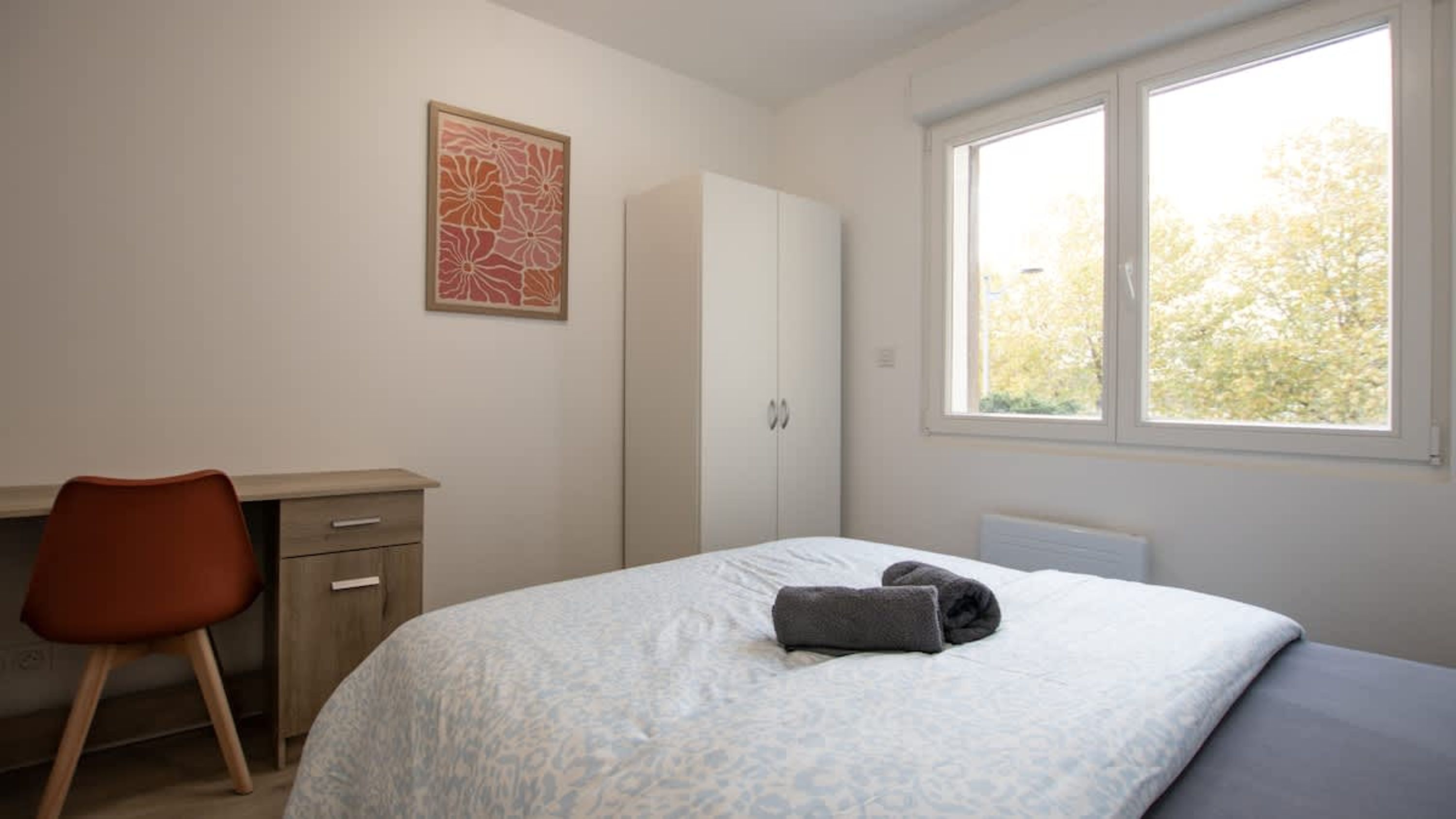 A bedroom with a bed, a desk, a chair, a wardrobe, and a window with a view of trees.