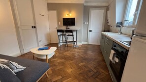 A compact kitchen with a dining area, a TV mounted above the counter, and a window providing natural light. - Appartement Central Avec Balcon (Arras)