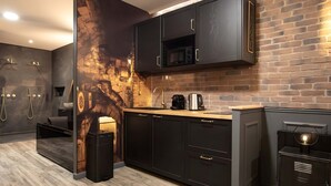 A modern kitchen with dark cabinetry, a brick wall, a built-in microwave, and a coffee maker. - La Suite des Arcades Grand Place Sauna et Balneo (Arras)