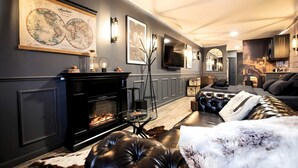 A modern living room with a fireplace, leather sofa, and a mounted television. - La Suite des Arcades Grand Place Sauna et Balneo (Arras)
