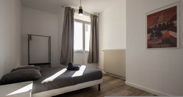 A bedroom with a bed, a radiator, a window with curtains, a standing lamp, and a poster on the wall. - Cosy Place d Armes au 3eme Etage (Douai)