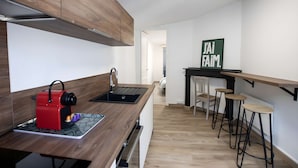 A modern kitchen with a wooden countertop, a red coffee machine, a black sink, and a bar area with stools. - Le Perchoir de Maurice Calme et Cosy (Arras)