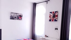 Un dormitorio con dos camas, un escritorio, una silla, una ventana con cortinas y un cuadro en la pared.