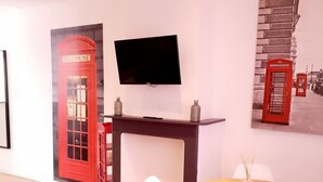 Una habitación moderna con una mesa redonda de madera, sillas blancas, un televisor de pantalla plana montado en la pared y una obra de arte que representa un teléfono rojo.