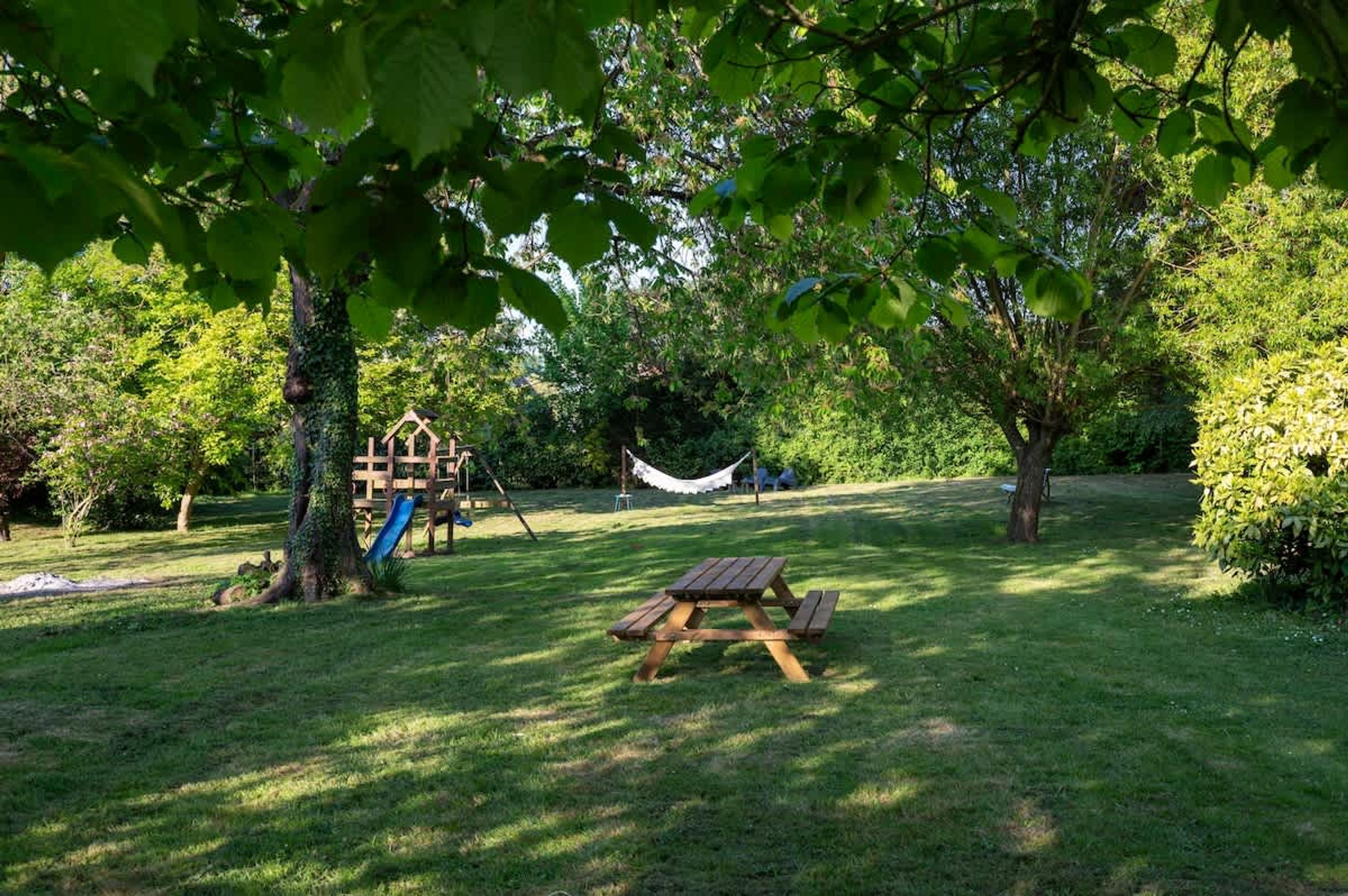 Un patio trasero con césped, una mesa de picnic, un columpio y una hamaca.