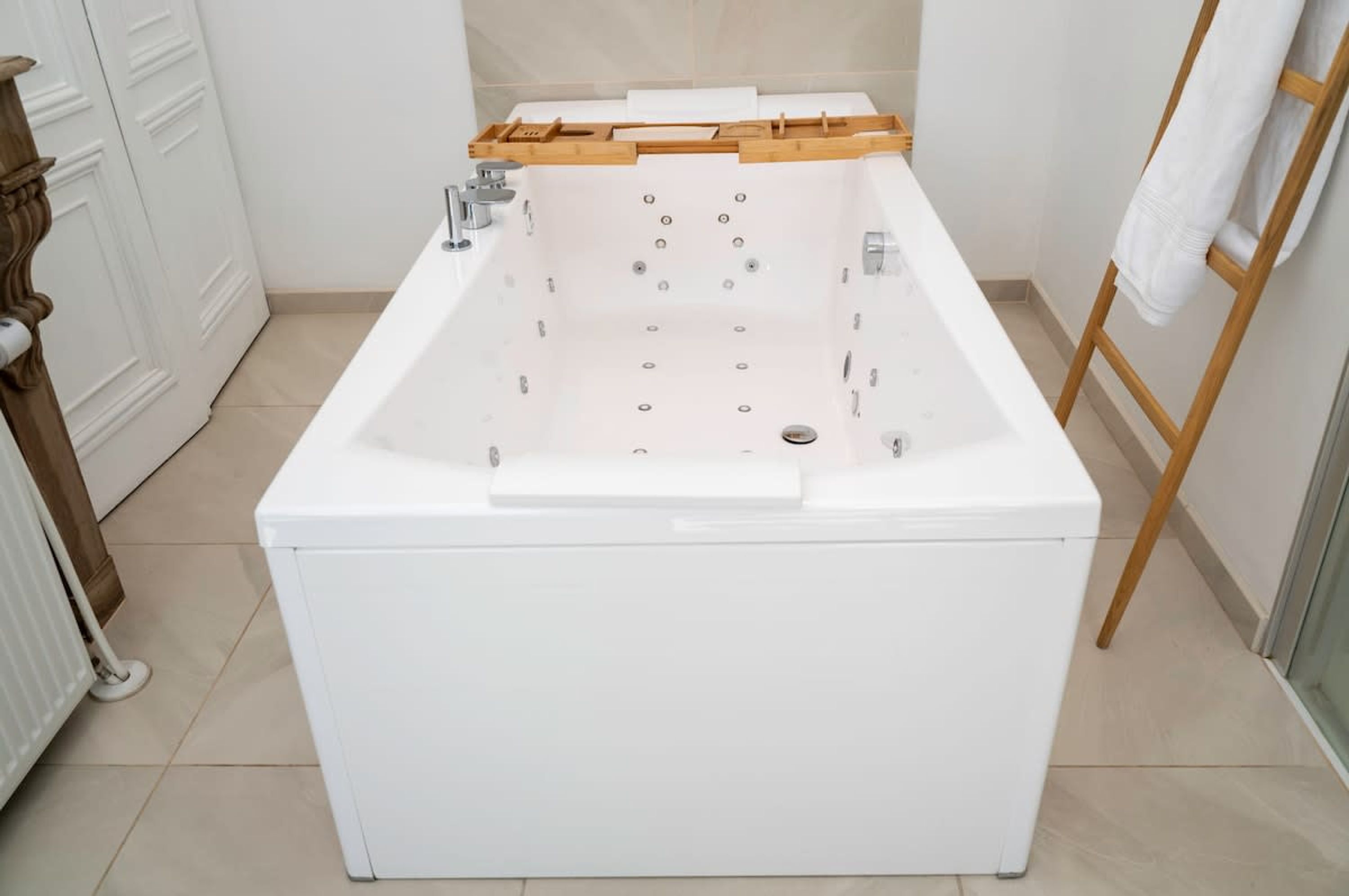 Et moderne badeværelse med et fristående badekar, et træhåndklædetørrestativ og en hvid radiator.
