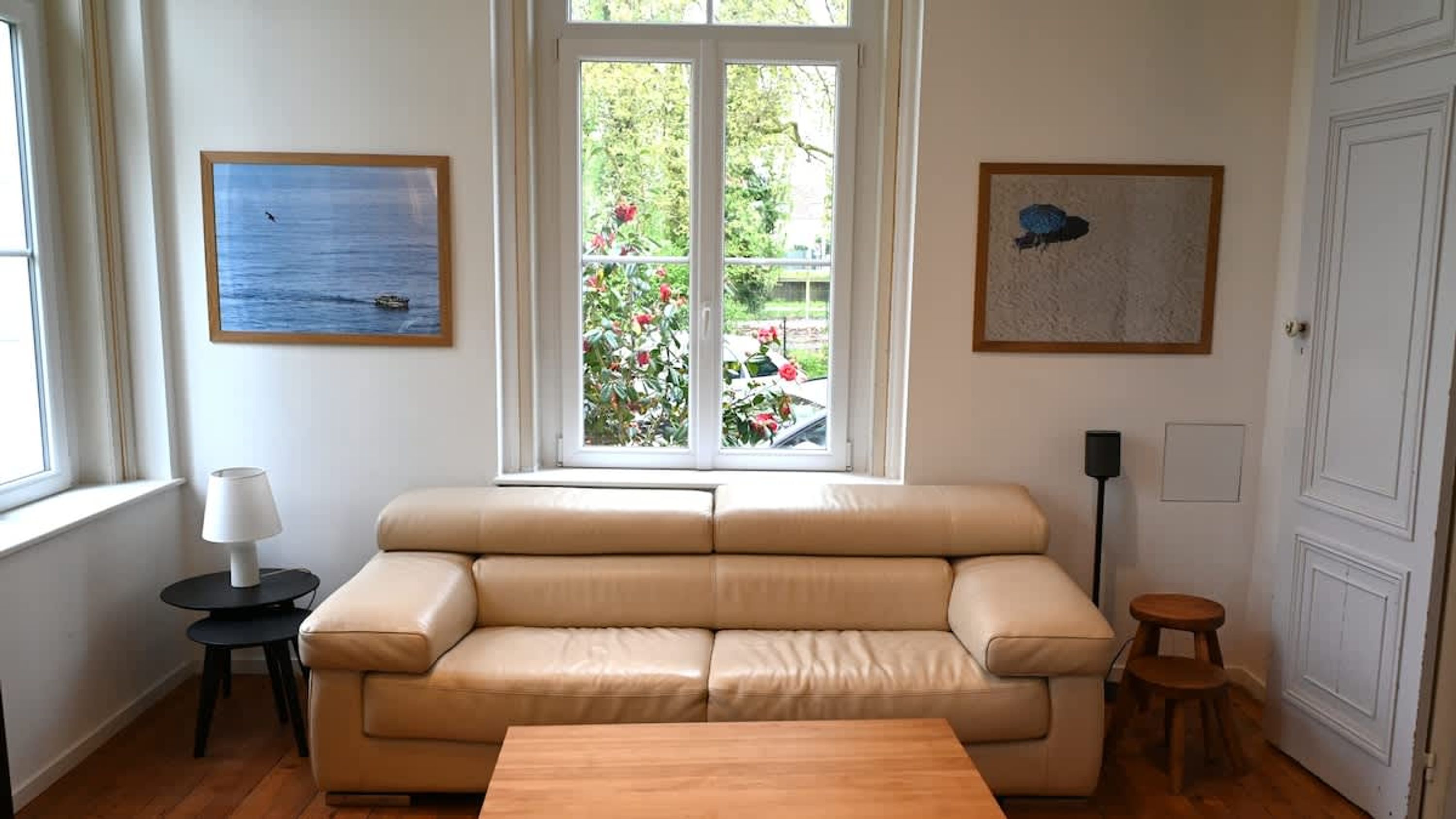 Una habitación con un sofá beige, una mesita, una lámpara y dos cuadros enmarcados en las paredes.