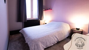 Un dormitorio con cama, ventana con cortinas, lámpara de noche y un logotipo en la pared.