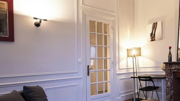 Una habitación con una puerta blanca, un sofá, una mesa, una lámpara y una chimenea.