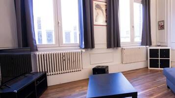 A room with a large window, a radiator, a black table, and a black sofa.