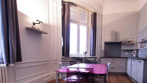Cocina compacta con mesa de comedor, ventana con cortinas y electrodomésticos integrados.
