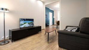 Un saló modern amb televisió de pantalla plana sobre un moble negre, un sofà de cuir, una taula de centre de fusta petita i una làmpada de peu.