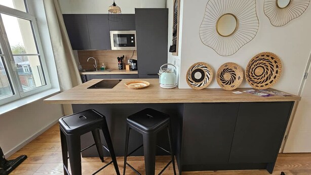 Una cocina moderna con encimera de madera, taburetes negros, un hervidor y platos decorativos tejidos.