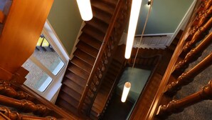 Una escalera de madera con barandilla, un accesorio de iluminación y vista a una habitación con ventana.