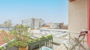 Terraza en la azotea con plantas en macetas, vistas despejadas de edificios circundantes y una pared roja.