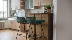 Una cocina con armarios de madera, un ventanal y dos sillas verdes.